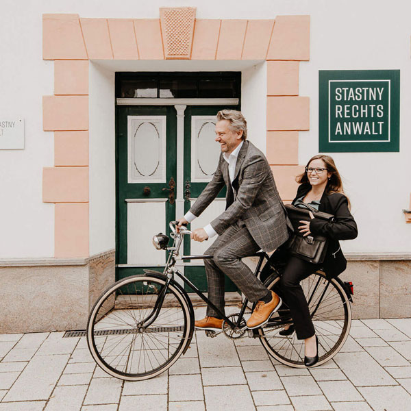 Dr. Stefan Stastny und Frau Mag. Tamara Wango fahren fröhlich mit dem Fahrrad vor der Kanzlei